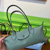 A light sage green storage shoulder bag with black handles resting on a wooden surface.