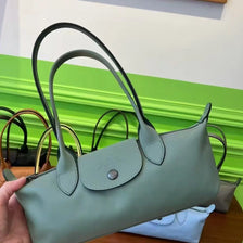 A light sage green storage shoulder bag with black handles resting on a wooden surface.