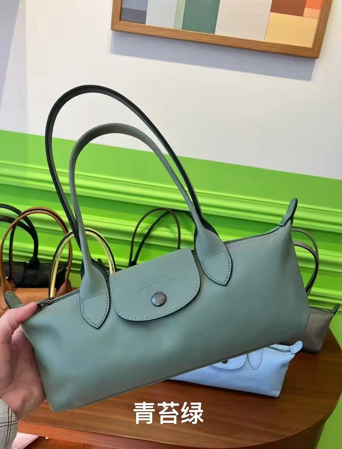 A light sage green storage shoulder bag with black handles resting on a wooden surface.