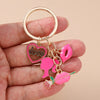 A hand holds a gold-colored enamel keychain featuring a heart and a pink rose design.