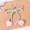 Aesthetic tulip flower bag charm keychain with a heart-shaped clasp and pearl strands on a light green ribbon.