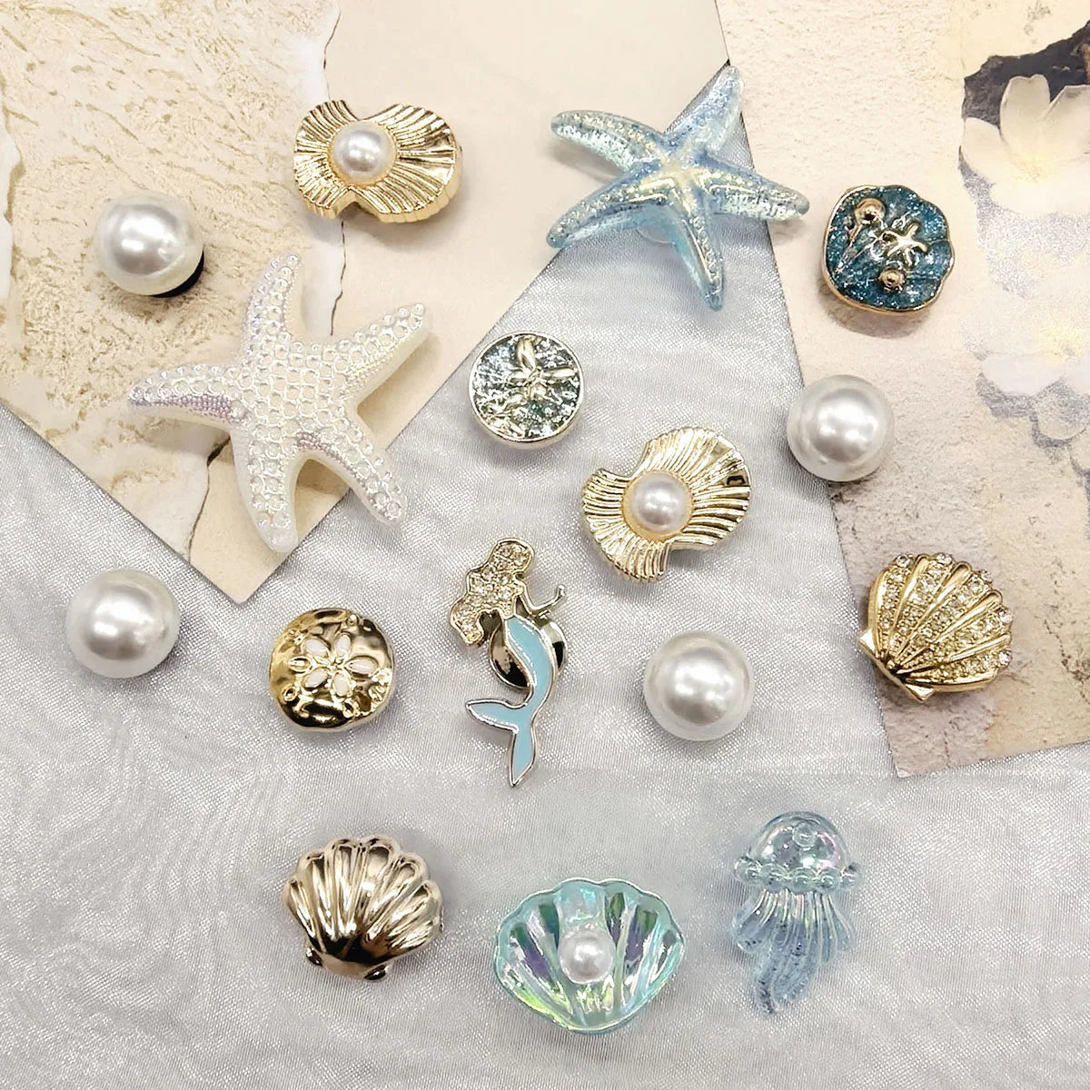 A collection of golden and silver sea-themed charms including starfish, conch shells, and pearl beads on a gray background.