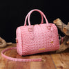A pink luxury crocodile pattern crossbody tote bag resting on a wooden surface.