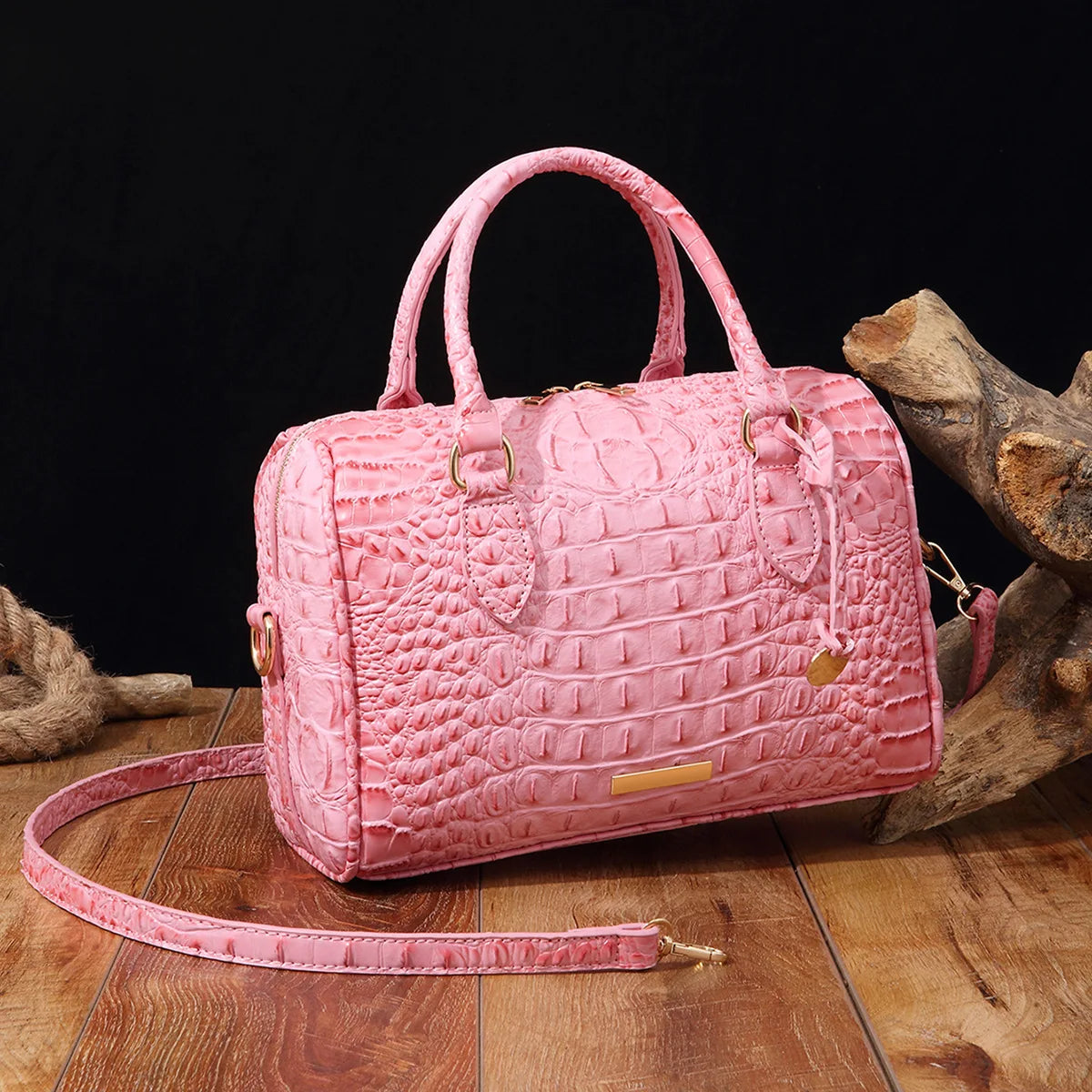 A pink luxury crocodile pattern crossbody tote bag resting on a wooden surface.