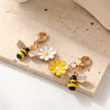 Gold-toned beaded flower keychains featuring white and yellow flowers and bee charms on a beige surface