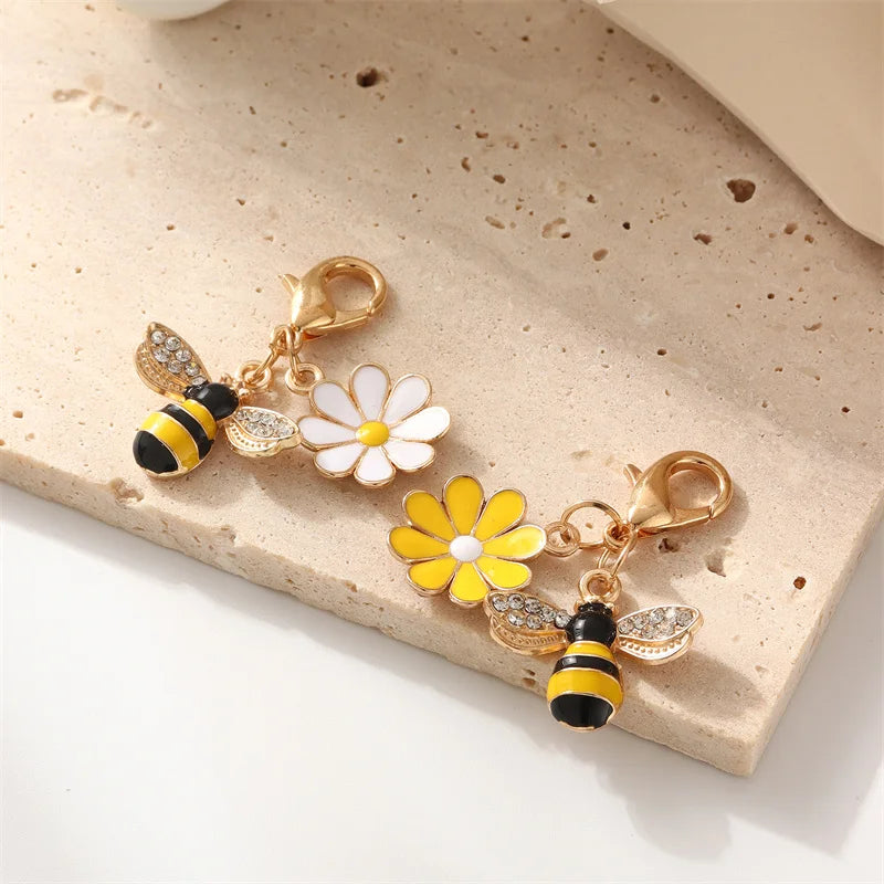 Gold-toned beaded flower keychains featuring white and yellow flowers and bee charms on a beige surface
