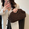 A woman holds a dark brown straw woven tote handbag against a white blazer.
