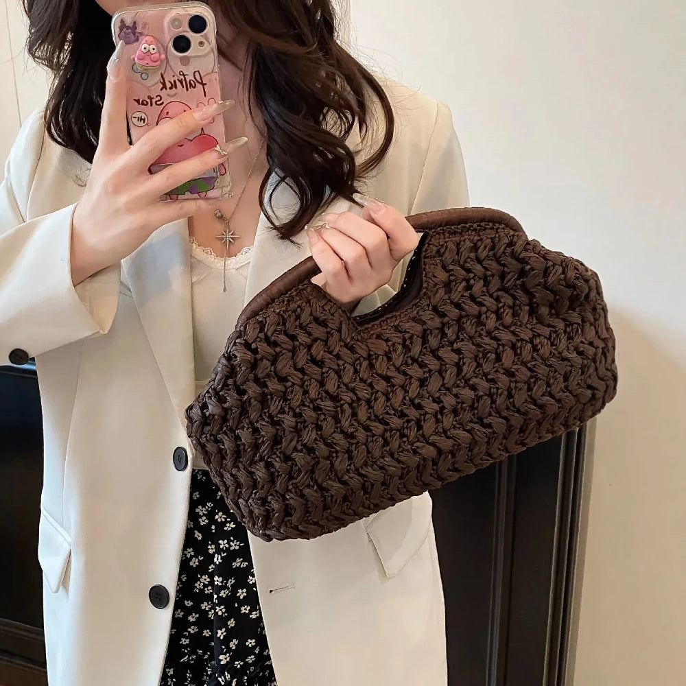 A woman holds a dark brown straw woven tote handbag against a white blazer.