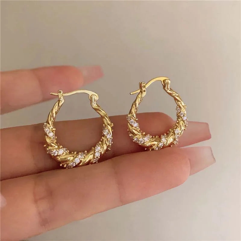 Goldene U-förmige geometrische Ohrringe mit strukturiertem geflochtenem Design, präsentiert auf einer Hand.