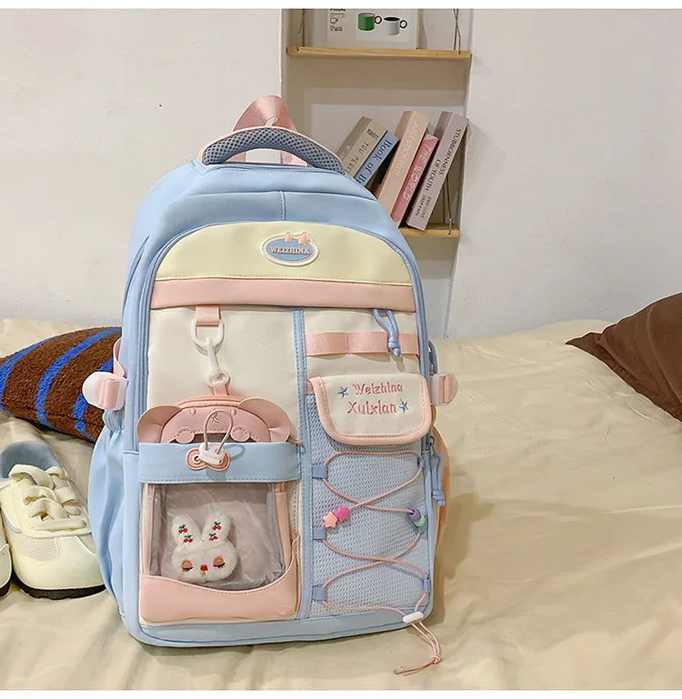 A light blue and pink Candy Color Campus backpack with a patterned fabric and storage pockets resting on a white surface.