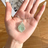 A hand holds a handcrafted amethyst crystal pendant necklace featuring a green crystal wrapped with copper wire.