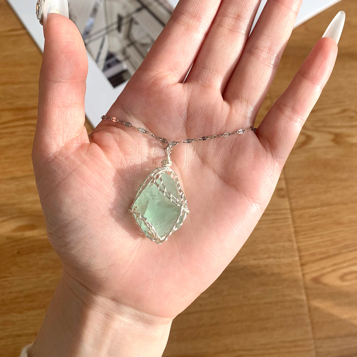 A hand holds a handcrafted amethyst crystal pendant necklace featuring a green crystal wrapped with copper wire.