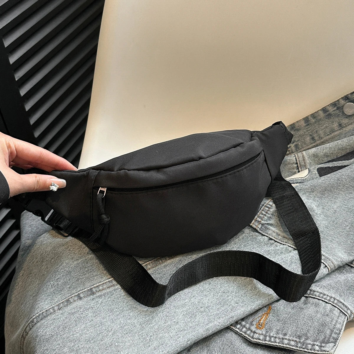 A black nylon crossbody sling bag is shown resting on a gray denim shirt.