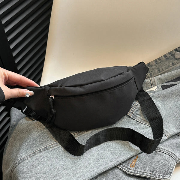 A black nylon crossbody sling bag is shown resting on a gray denim shirt.