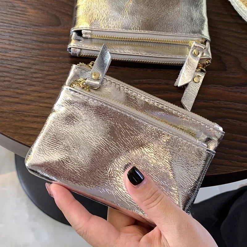 A hand holds a silver metallic leather compact coin purse and key holder on a dark wooden surface.