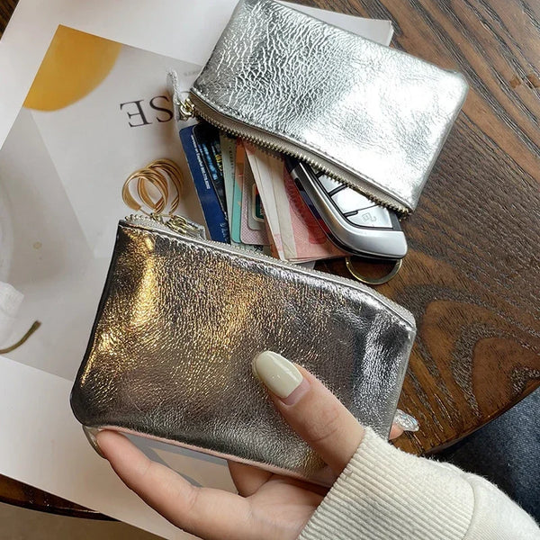 A hand holds a silver metallic leather compact coin purse and key holder with various coins and keys visible.