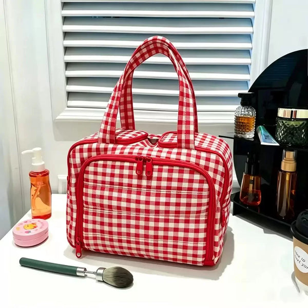A red and white checkered travel cosmetic organizer pouch with a zipper and handles is displayed on a white surface.