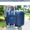 A blue foldable travel duffel bag is shown being carried by a person outdoors.