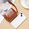 A brown vintage PU leather compact wallet with a leather strap resting on a beige surface next to a white smartphone.