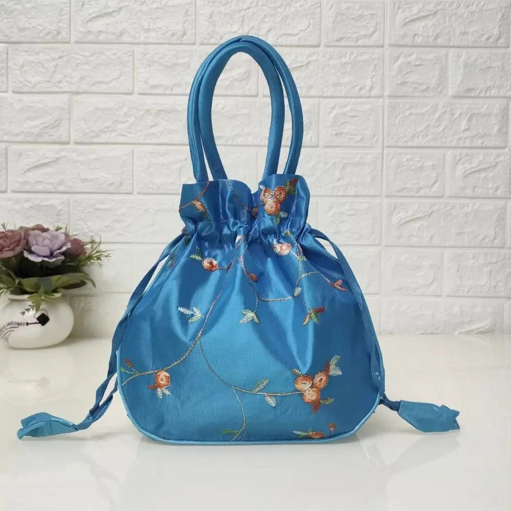 Clutch de fiesta azul brillante de satén con lazo bordado floral sobre una superficie blanca.