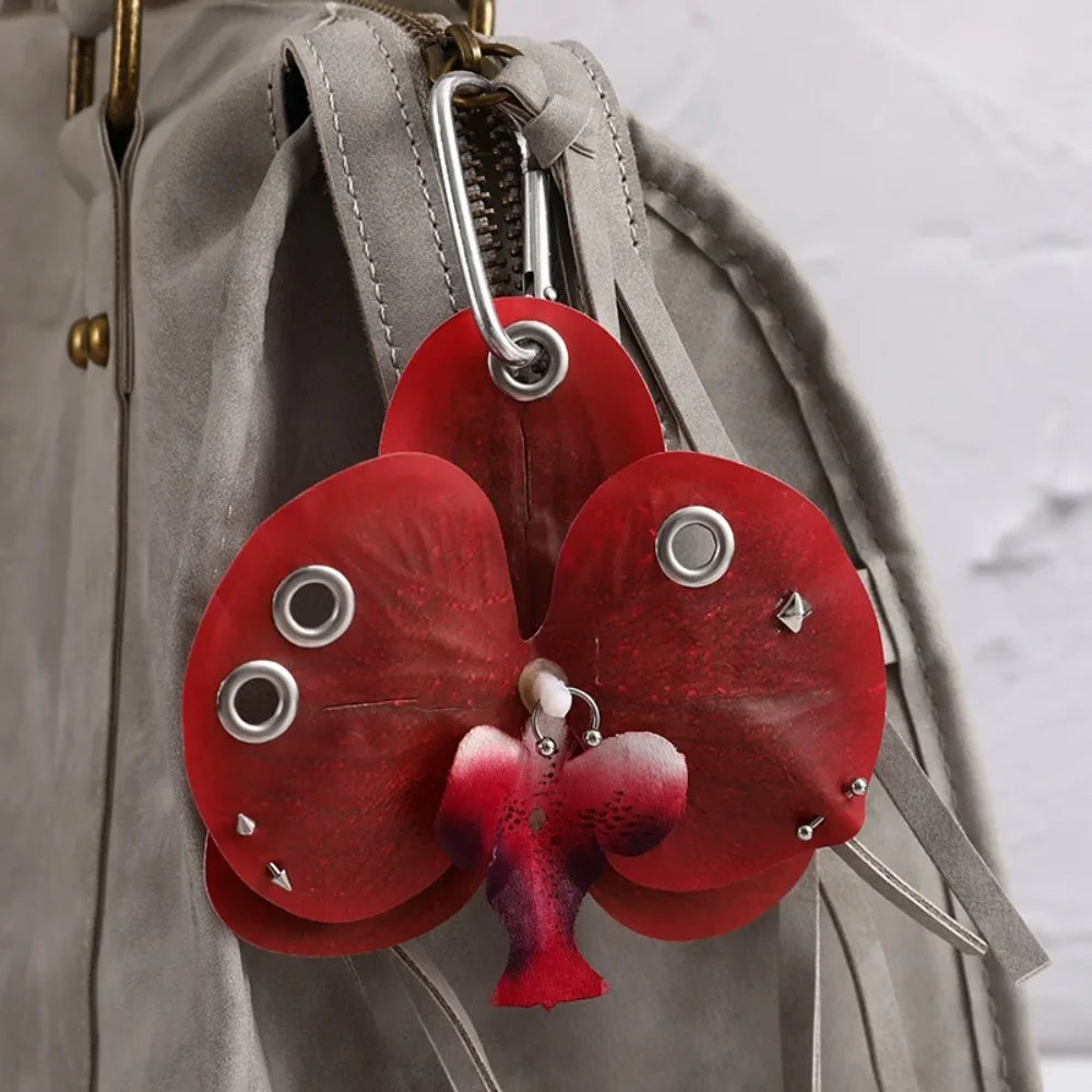 A red orchid flower keychain attached to a gray fabric bag.