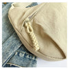 A beige soft nylon crossbody shoulder bag is shown with a drawstring closure and a light wash denim jacket in the background.
