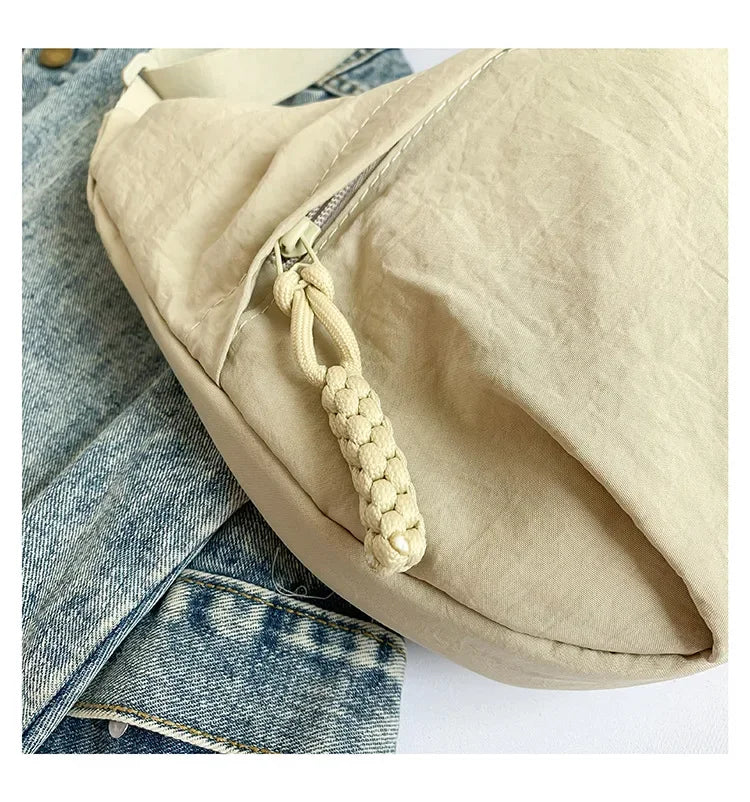 A beige soft nylon crossbody shoulder bag is shown with a drawstring closure and a light wash denim jacket in the background.