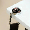 A silver bag hook with a floral pattern is displayed on a white surface.