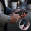 A hand holds a black carbon fiber microfiber wallet with an orange accent, shown against a blurred background.