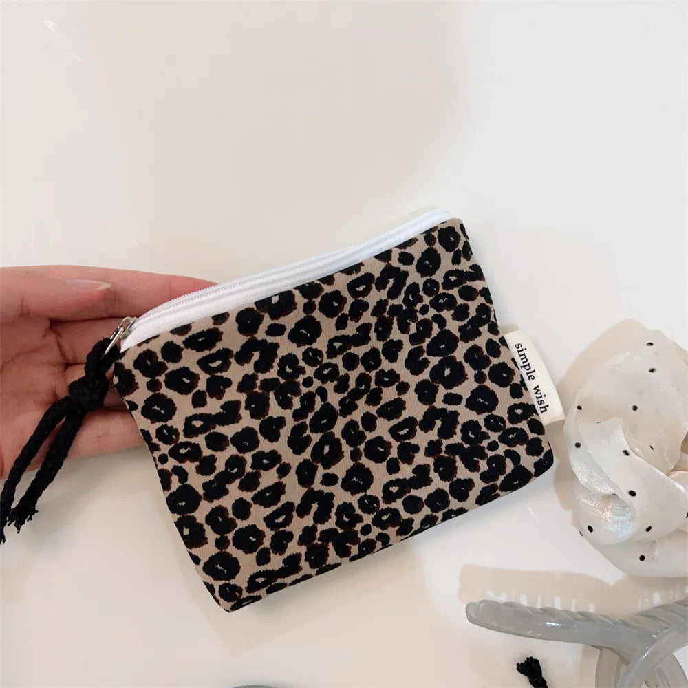 A black leopard print cosmetic pouch with a zipper and a small tag is held in a hand.