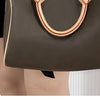 A brown leather handbag with a red trim strap is shown being held by a person.