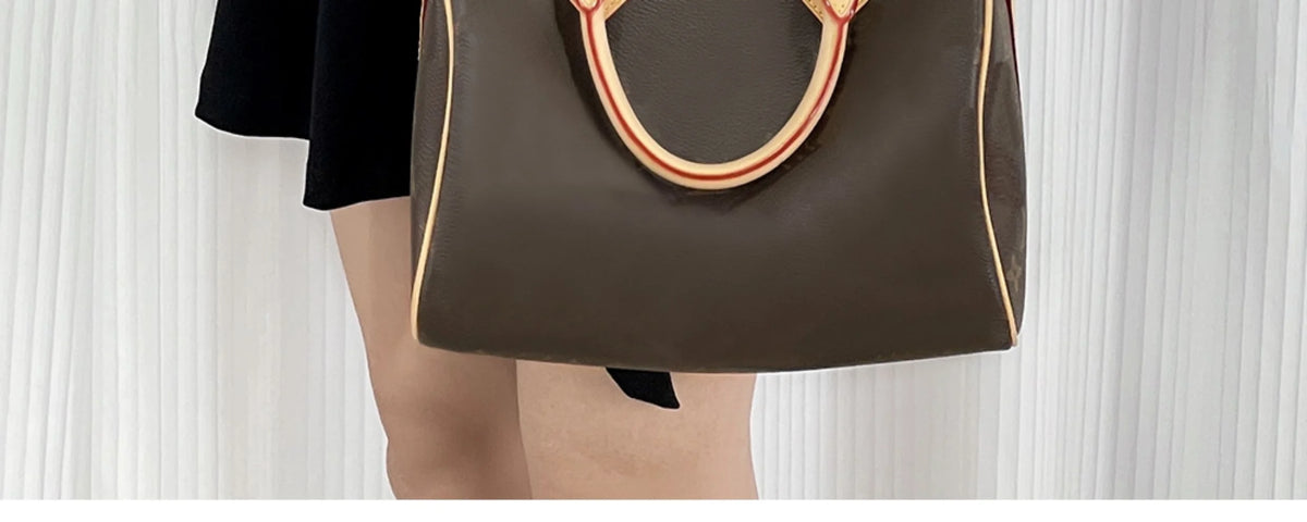 A brown leather handbag with a red trim strap is shown being held by a person.
