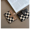 A black and beige checkered PU leather mini card wallet resting on a brown surface next to a piece of paper.