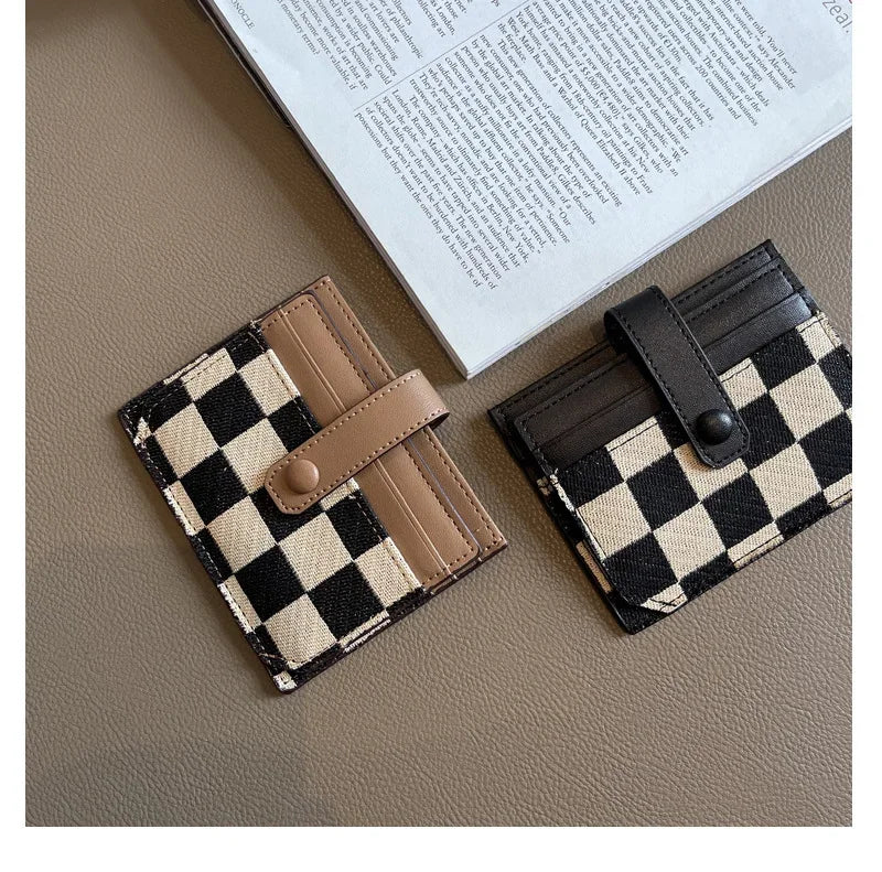 A black and beige checkered PU leather mini card wallet resting on a brown surface next to a piece of paper.