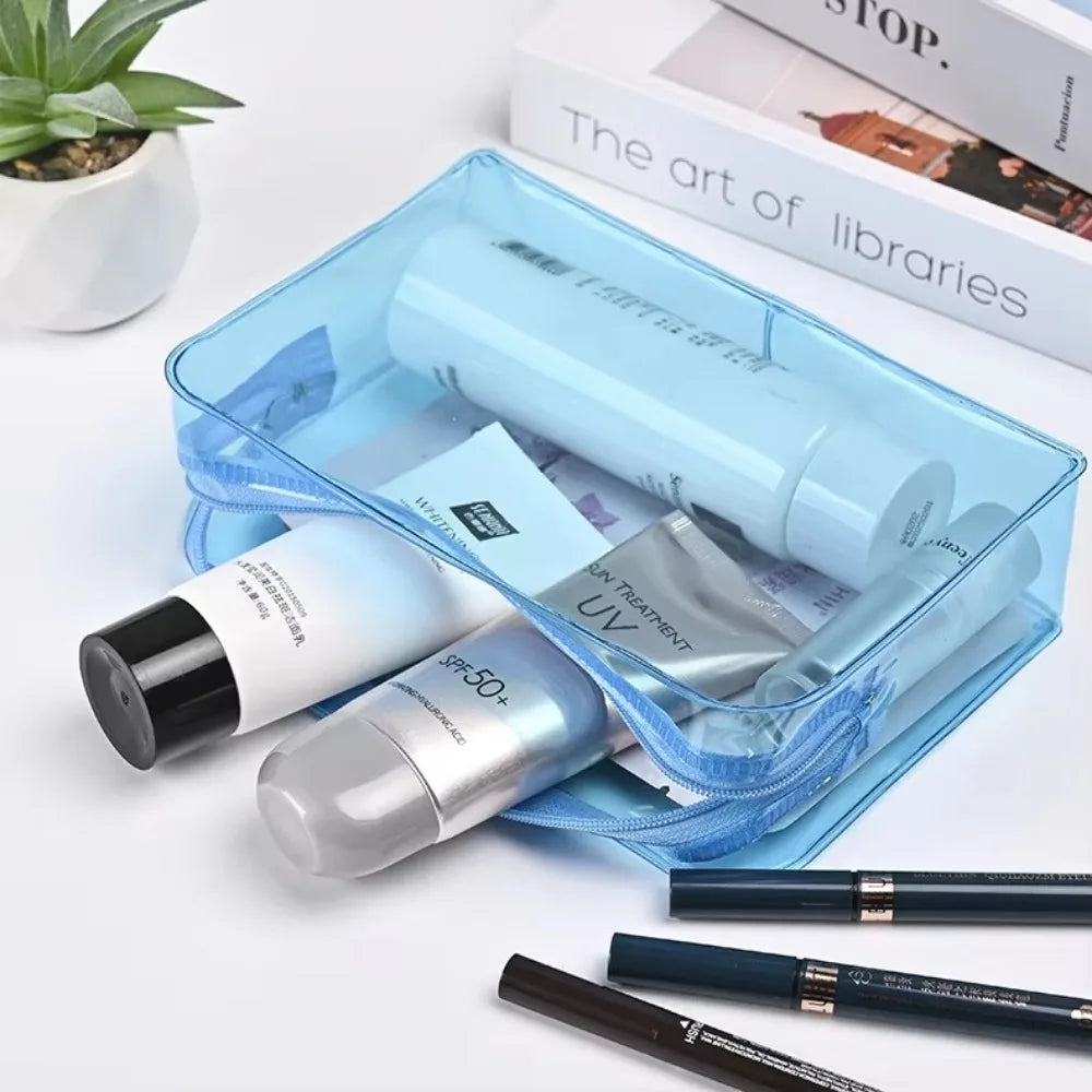 A transparent blue PVC travel makeup bag containing various cosmetic products and lipsticks.