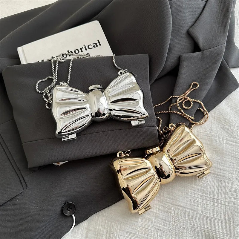 Silver and gold acrylic bow clasps with chain straps displayed on a dark gray envelope.
