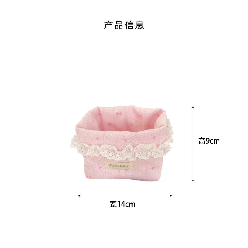 Light pink fabric storage basket with a delicate lace trim featuring heart and bow patterns.