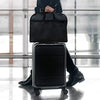 A black portable fabric clothes dust cover and storage bag is shown standing on a rolling suitcase.