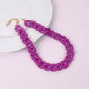 A purple acrylic statement choker necklace with a gold-tone chain is displayed on a white plate.