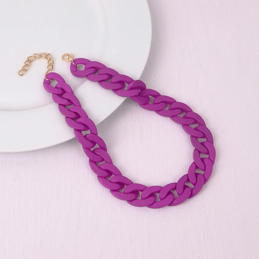 A purple acrylic statement choker necklace with a gold-tone chain is displayed on a white plate.