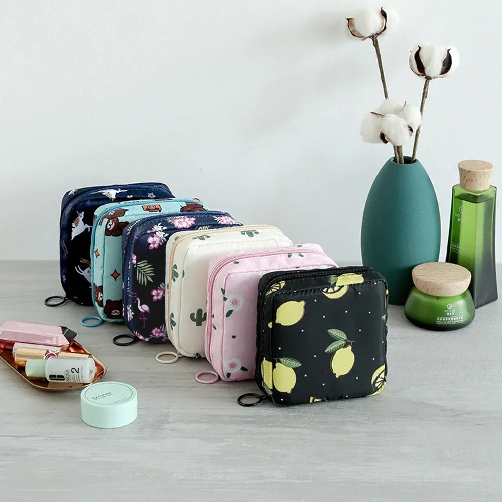 A collection of cute, floral-patterned sanitary pad storage pouches and a green glass jar with white cotton stems.