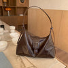 A brown retro PU leather underarm bag with a long strap rests on a light surface next to a beige fabric.