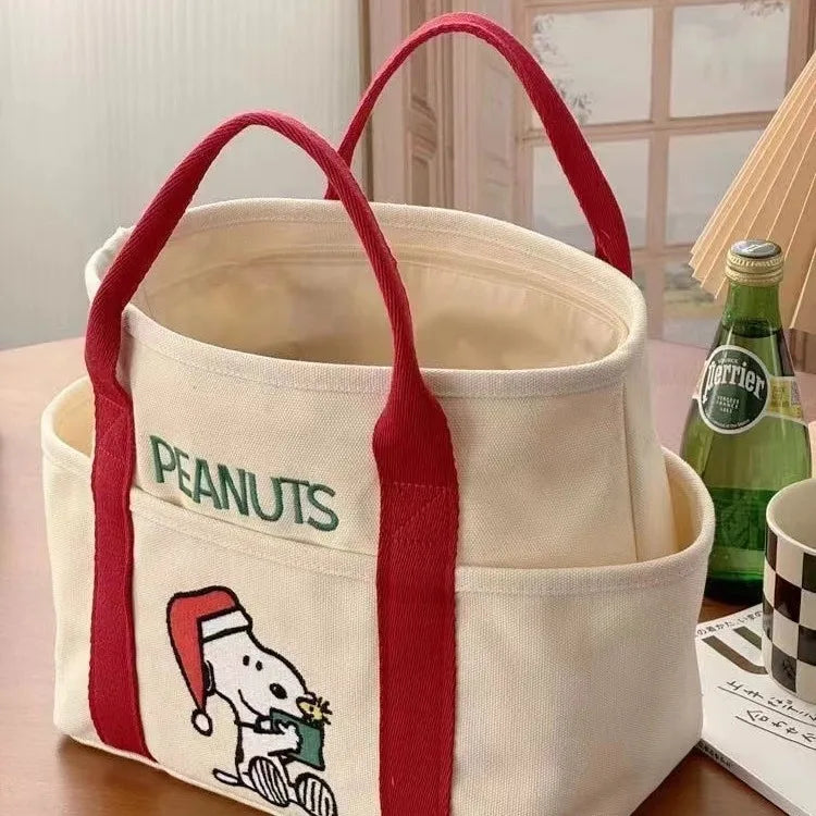 A beige canvas shoulder bag with red handles and a Snoopy cartoon design on the front.