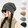 A woman wearing a gray slouchy knit beanie hat with dark sunglasses and a gold chain necklace.