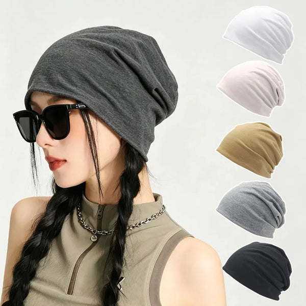 A woman wearing a gray slouchy knit beanie hat with dark sunglasses and a gold chain necklace.