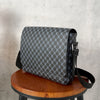 A dark gray patterned flap crossbody bag resting on a wooden stool.