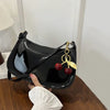 A black PU leather shoulder bag with a gold chain and a red cherry pendant is being held by a hand.