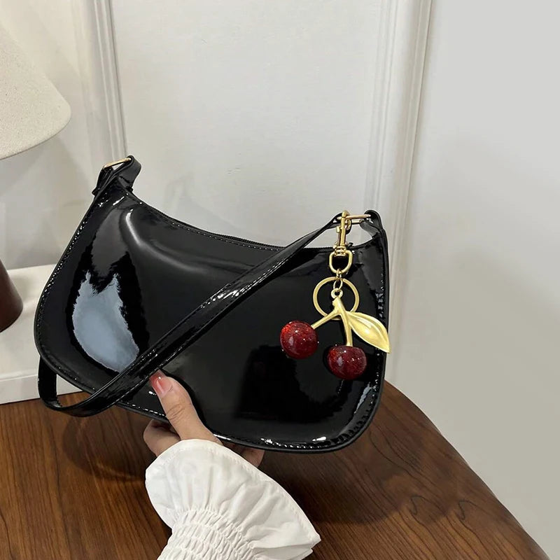 A black PU leather shoulder bag with a gold chain and a red cherry pendant is being held by a hand.