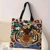 A canvas tote bag featuring an illustration of a tiger head surrounded by a wreath of floral and foliage elements in leopard 