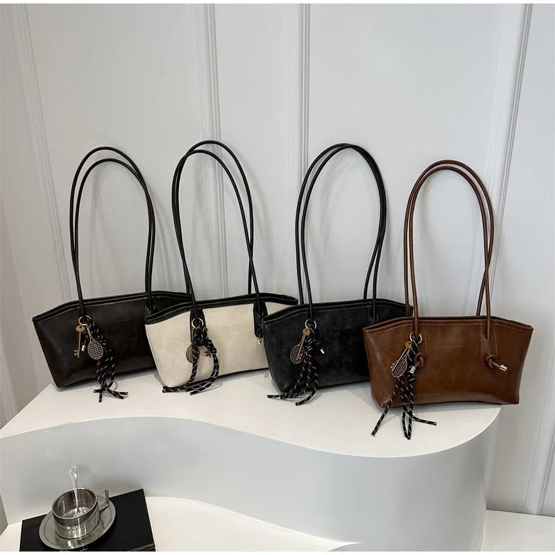 A row of four black and brown leather tote bags with long handles displayed on a white surface.
